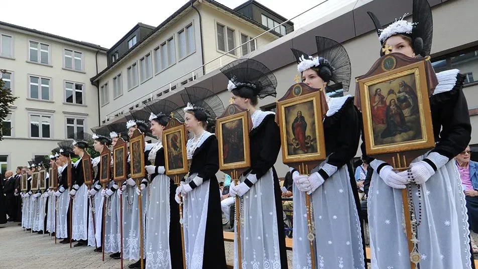 Reihe von Frauen in schwarz-weisser Appenzeller Tracht trägt gerahmte religiöse Bilder in der Fronleichnamsprozession.