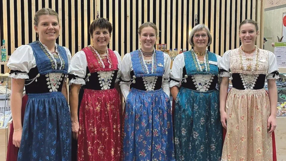 Fünf Frauen in Appenzeller Festtagstracht mit besticktem Mieder und geblümter Schürze an einem Messestand.